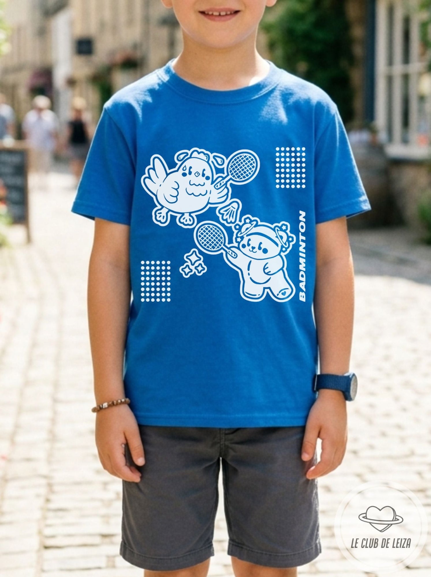 Child wearing a blue t-shirt with white graphics and text, standing on a street.