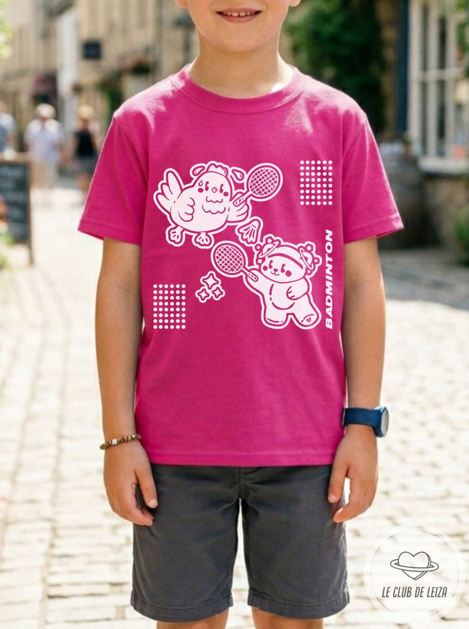 Child wearing a pink t-shirt with cartoon characters and text, standing outdoors.